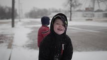 Happy young boy playing in cinematic slow motion in the snow while it's snowing outside on Christmas morning smiles at camera and laughs.