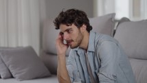 Disappointed young man sitting on couch thinking looking out the window feels moral badly after quarrel fight with wife, break up or divorce marriage split, unpleasant events in life suffering concept
