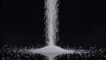 Pouring white sugar on black background in slow motion 