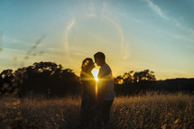 a couple standing together in a field at sunset 