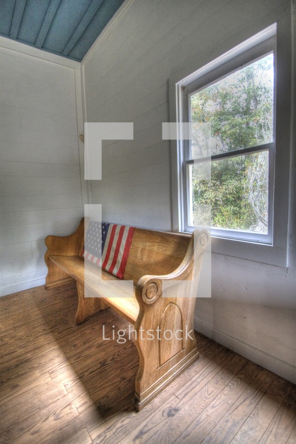 American flag on the back of a pew near a window.