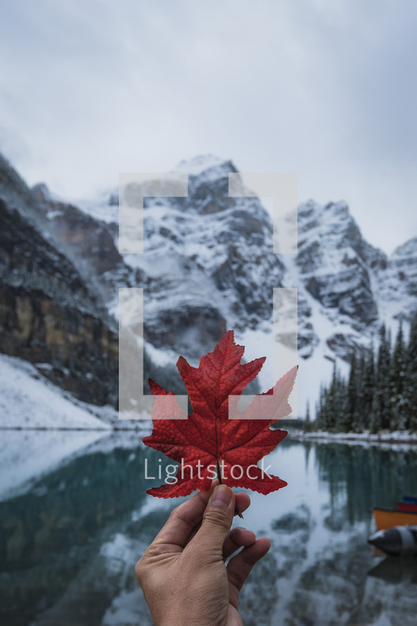 a person holding up a red leaf in front of Moraine Lake 