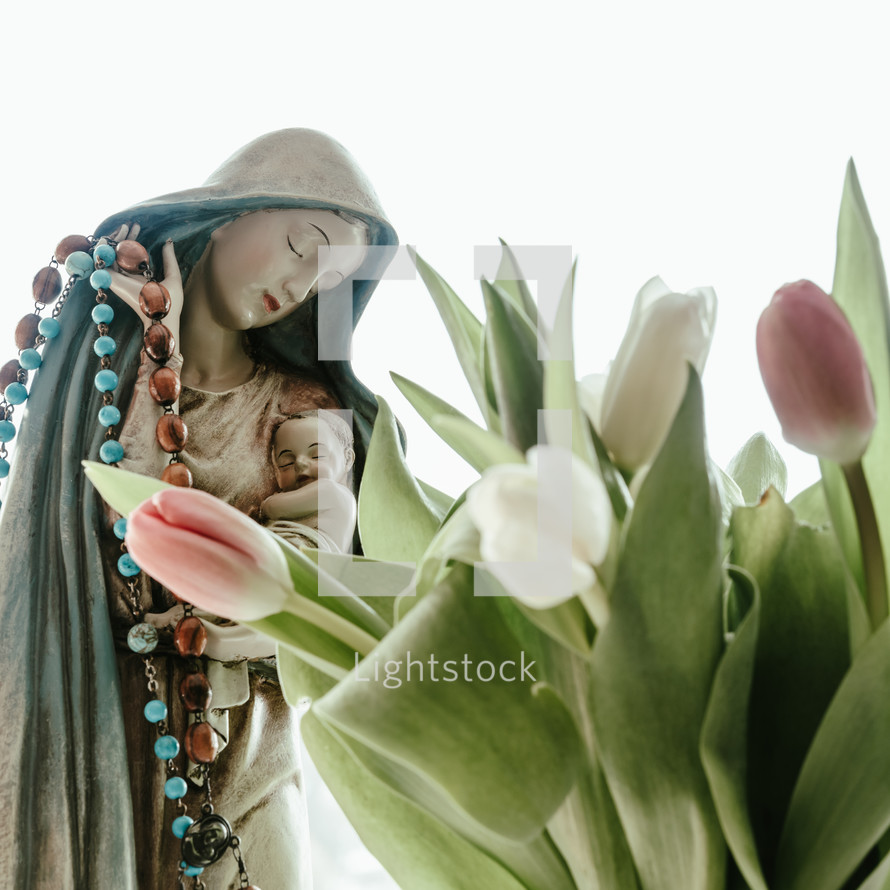 statue of Mary and Jesus holding a rosary and tulips 