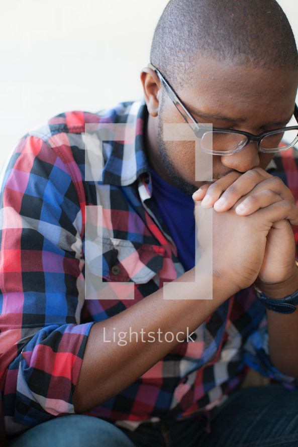 African-American man with glasses and praying hands and head bowed 