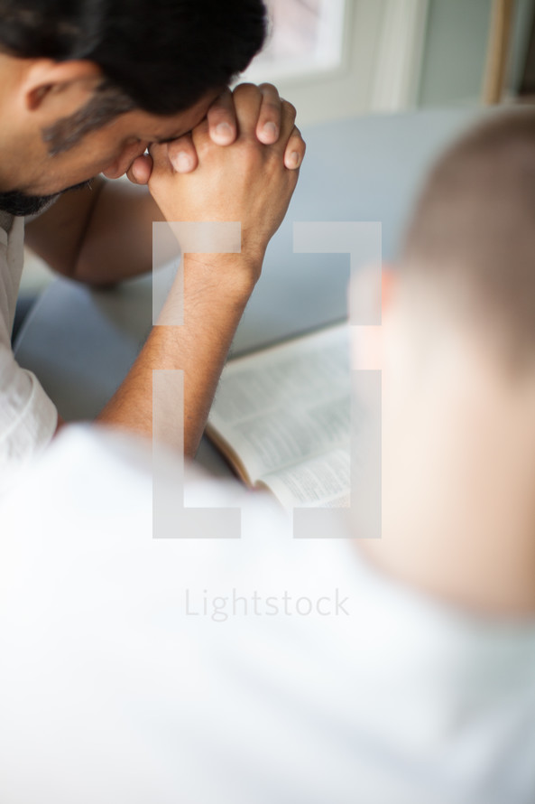 Two men at a table bowing their heads over an open Bible.