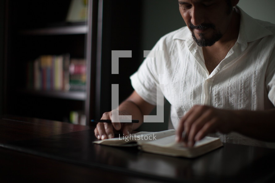 Man with a pen turning the pages of a Bible on a wooden table.