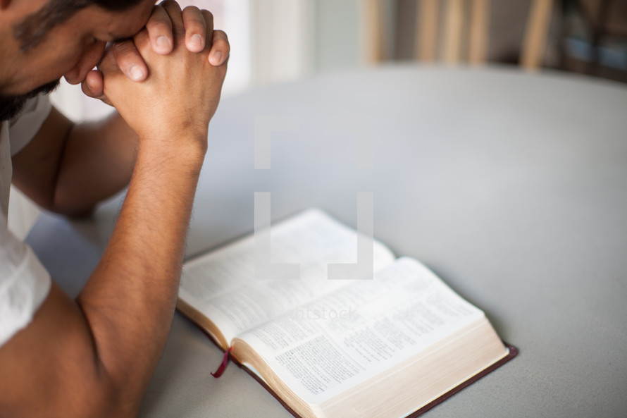 man with head bowed in prayer over a Bible