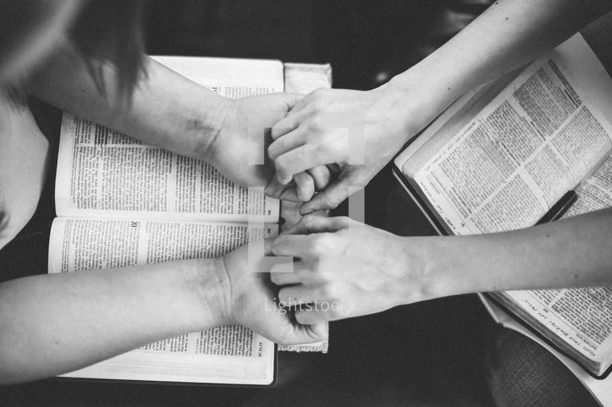 woman holding hands in prayer over a open Bible