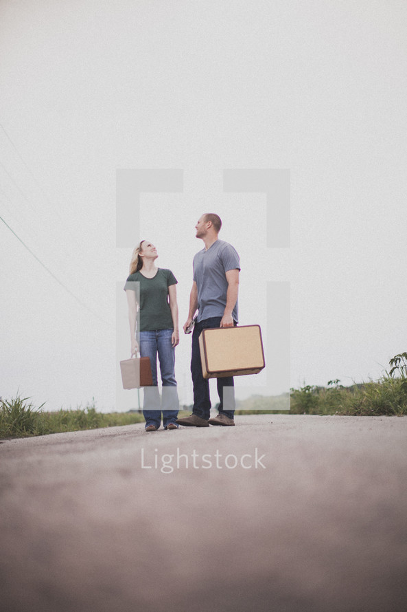 man and woman carrying luggage standing in the road