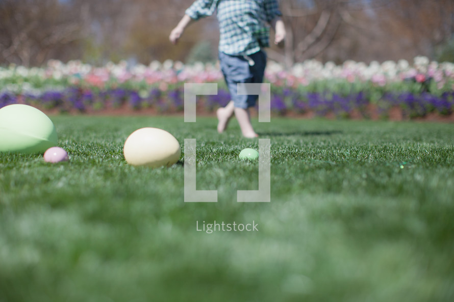 young boy running  through a garden  with Easter eggs laying on the ground