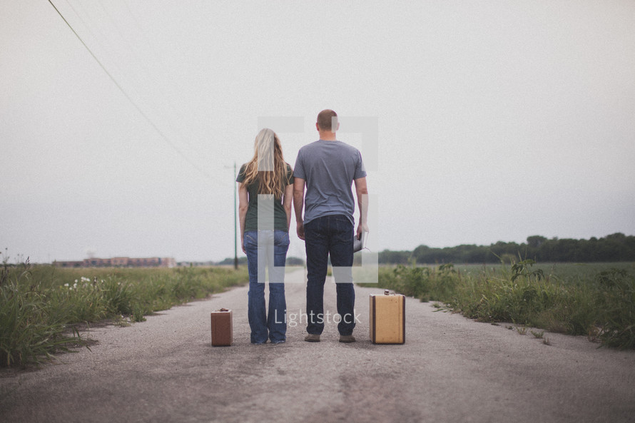 man and a woman standing in the middle of a road next to suitcases