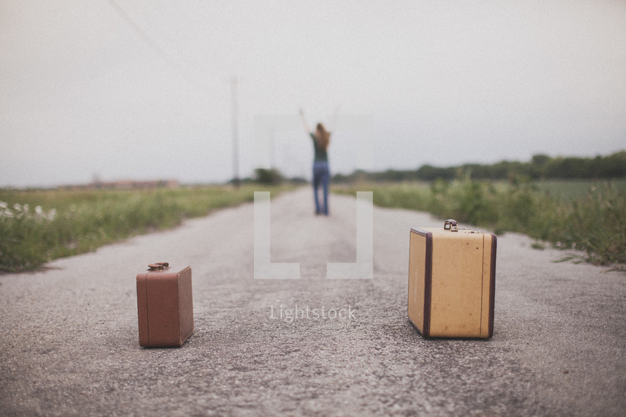 woman standing with her arms raised in the middle of a road in front of suitcases