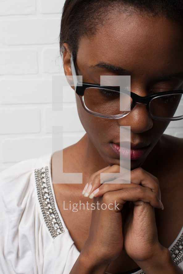 face of an African-American woman with reading glasses and praying hands 