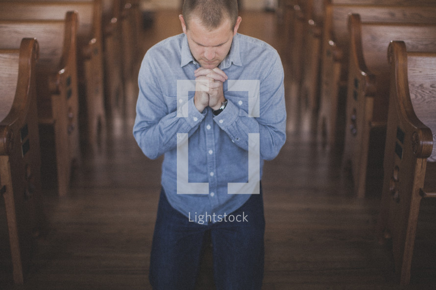 man kneeling in prayer in the aisle of a church 