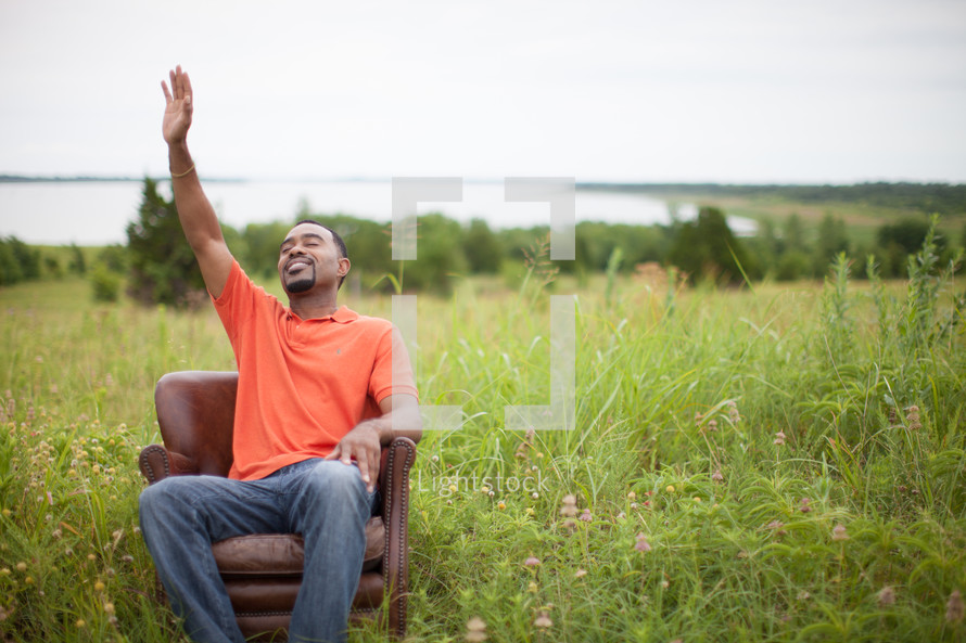 man sitting in a chair with hand raised to God outdoors 