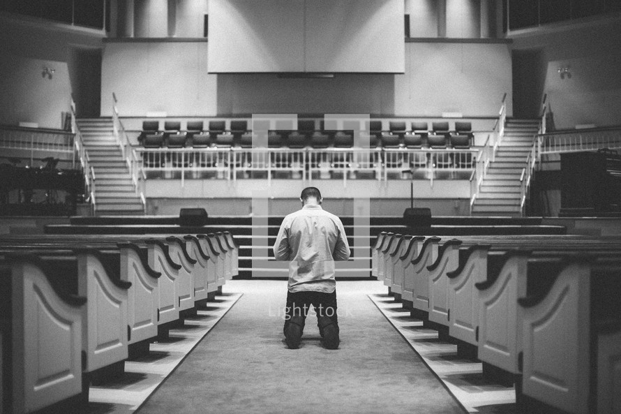man kneeling in the aisle of a church in front of the altar 
