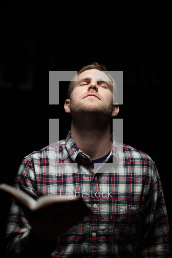 A man holding a Bible and closing his in prayer to God