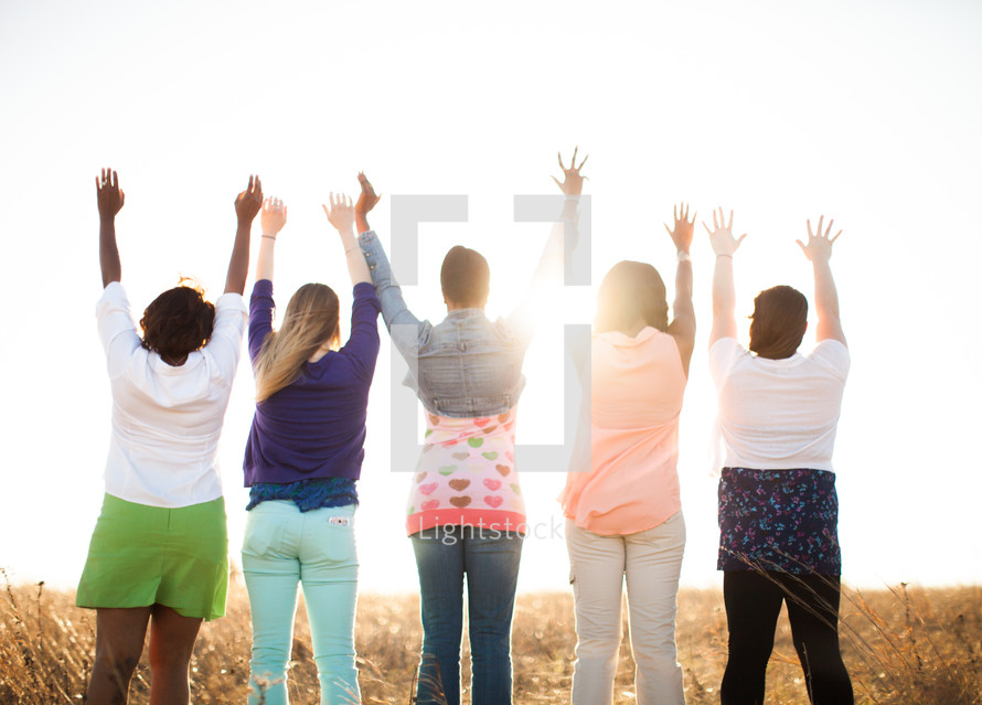 women with raised hands standing outdoors in a field 