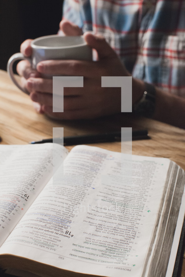 man holding a cup of coffee reading a Bible 