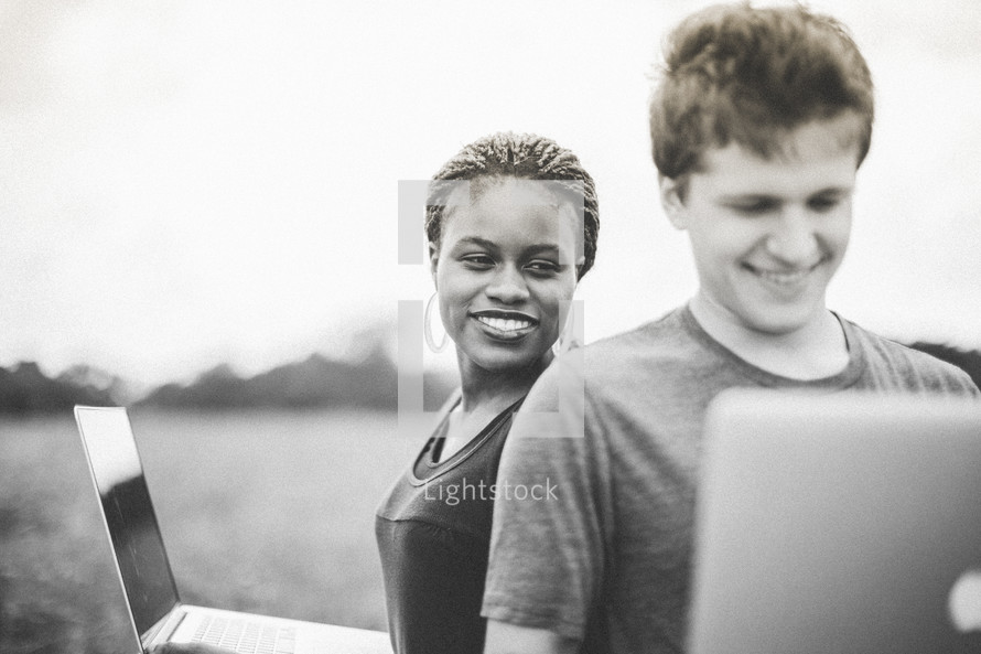man and woman looking at laptops outdoors 