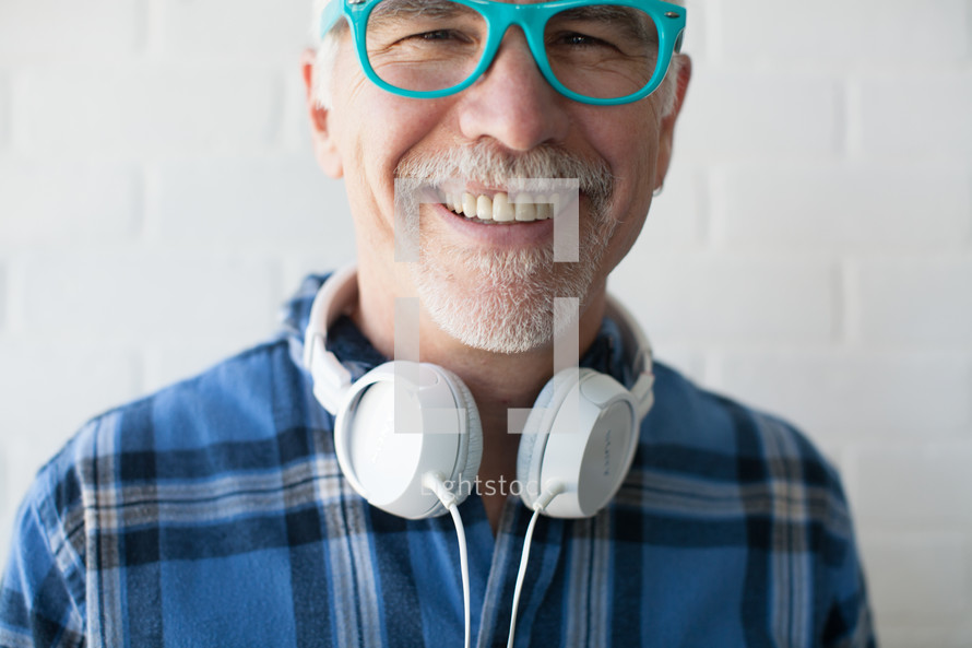 face of a man wearing reading glasses and headphones around his neck  with a white beard 