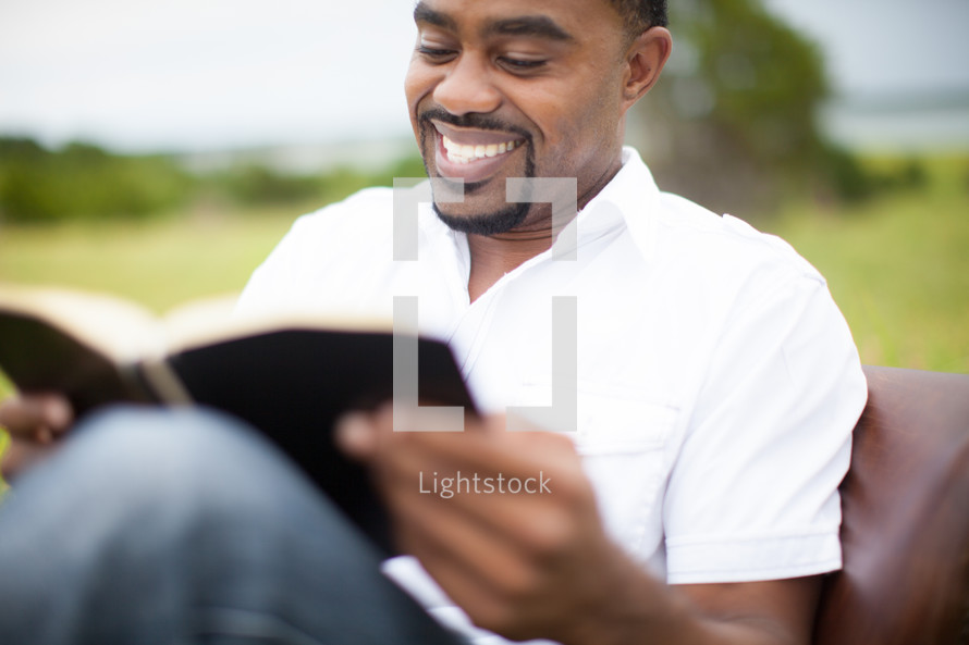 man reading a Bible sitting in a chair outdoors 