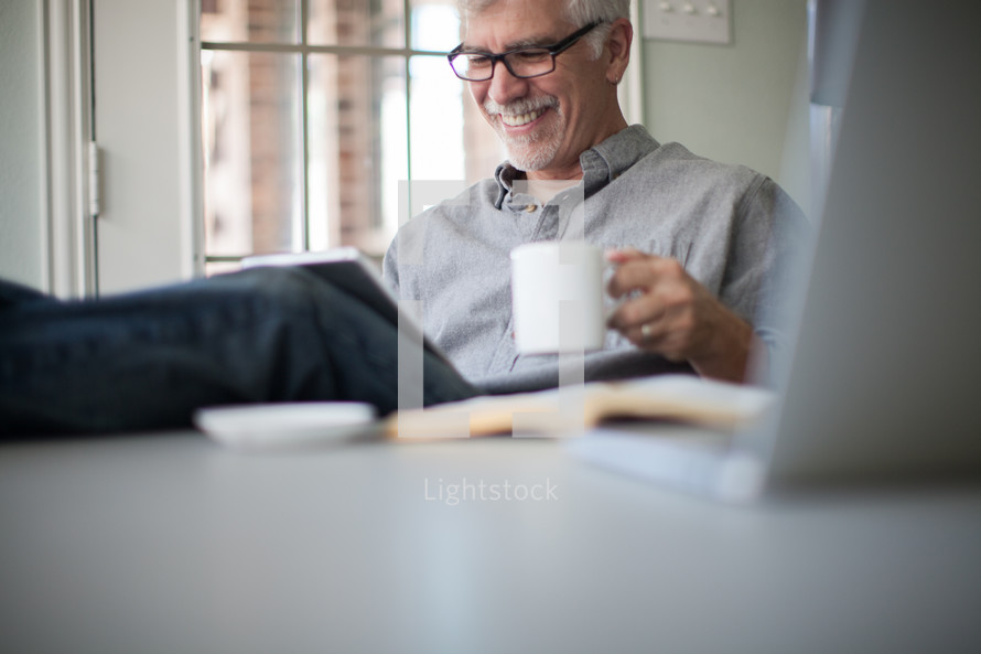 man looking at an iPad screen and drinking coffee 