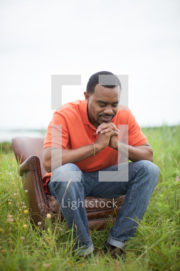African-Amrican man sitting in a chair in a field with praying hands 