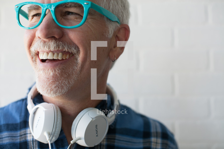 face of a man wearing reading glasses and headphones around his neck with a white beard 