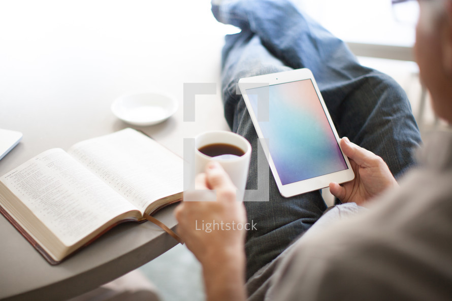 man looking at an iPad screen and an open Bible 