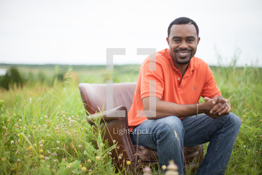 man sitting in a chair outdoors smiling with clasped hands 