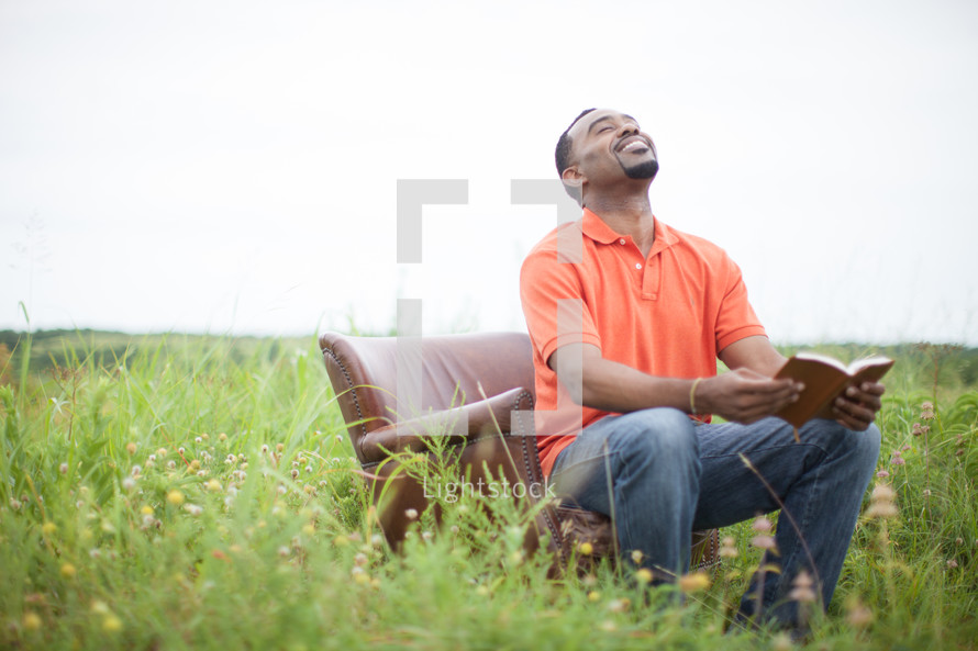 man sitting in a chair outdoors reading a Bible 