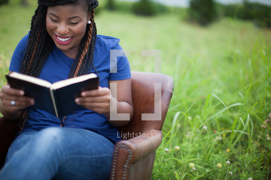 woman sitting in a chair outdoors reading a Bible 