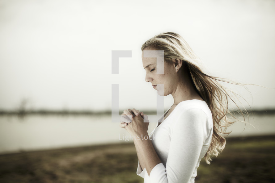 A young woman praying at the edge of a lake