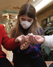 A girl is using antibacterial hand sanitizer while wearing a face mask to prevent a virus in a public area.