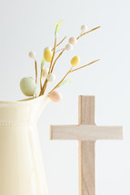 Decoration sprig with easter eggs and cross in a yellow pitcher with copy space