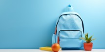Blue school backpack, notebook and apple on white table with blue wall background