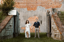 a couple holding hands standing in front of a brick wall 