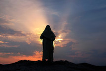 Jesus praying alone on a hill at sunset with rays. Biblical concept.
