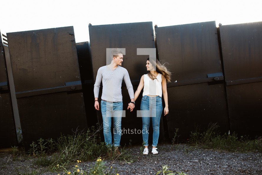 a couple holding hands in front of a metal wall 
