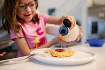Little girl pouring syrup on her pancakes 