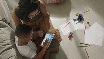 Latina mother cute little preschool son at home play on wireless tablet device. Smiling mom small kid boy look at pad screen have fun together use modern electronic tech concept