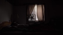 Young man, teen boy sitting on his bed. Silhouette of a teenager sitting in his bedroom at night on his bed.