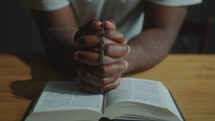 Hands of Man Holding Rosary Beads with Crucifix and Praying with Holy Bible