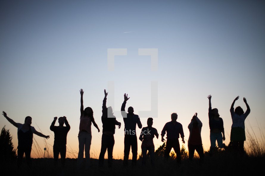 silhouettes of people with raised hands outdoors at dusk 