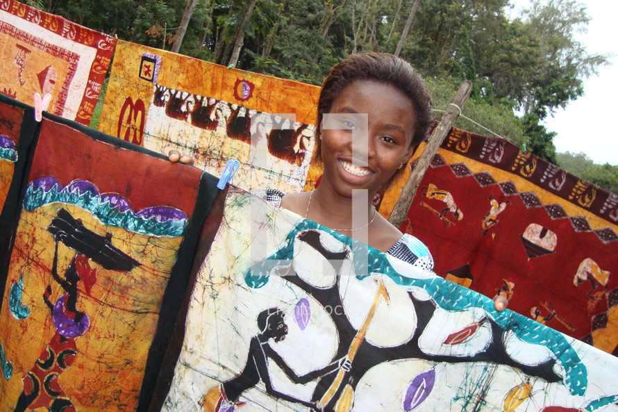 African girl smiling behind artwork at a batik market