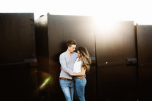 a couple snuggling in front of a metal wall 