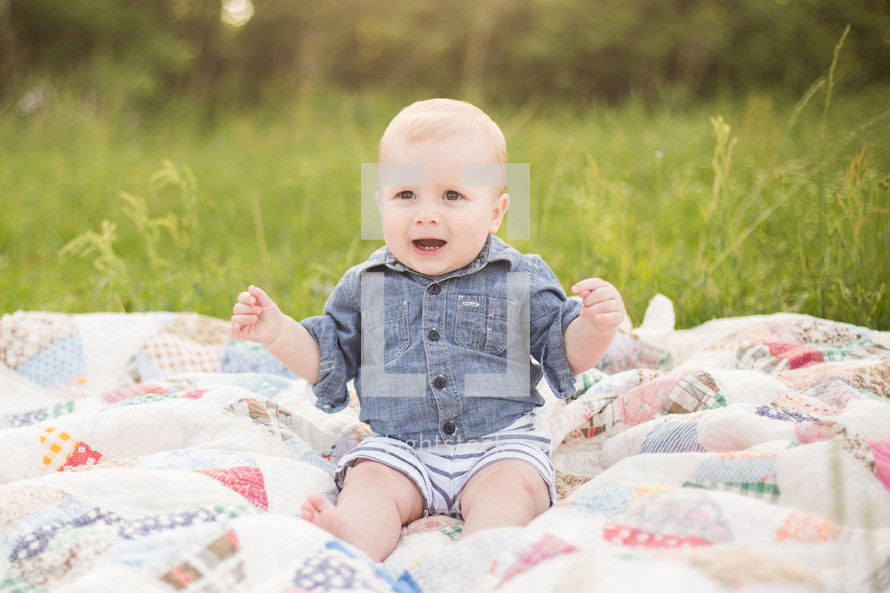 an infant boy sitting on a blanket in the grass 