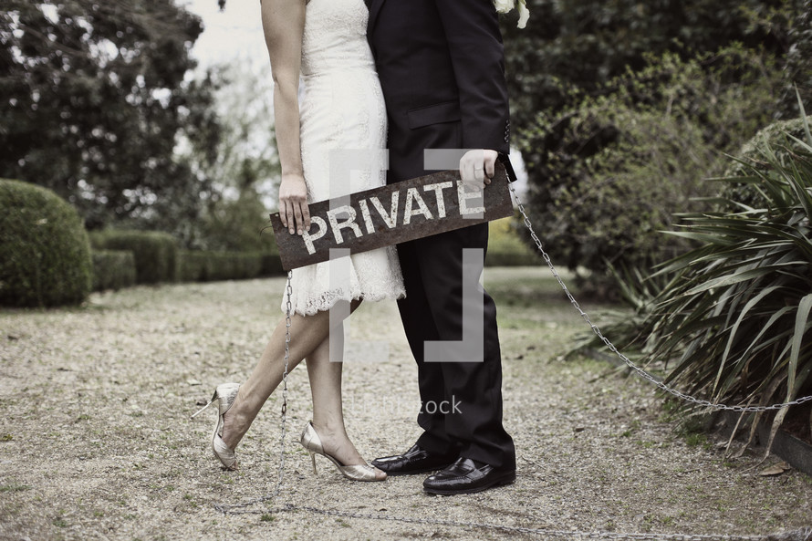 torso of bride and groom holding a private sign