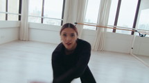 Young smiling girl approaching the camera camera, performing energetic movements and jumps during expressive contemporary dance in studio. Handheld zoom-out shot
